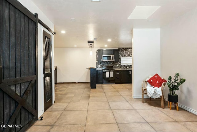 kitchen with tasteful backsplash, stainless steel microwave, black gas range, a barn door, and light tile patterned floors