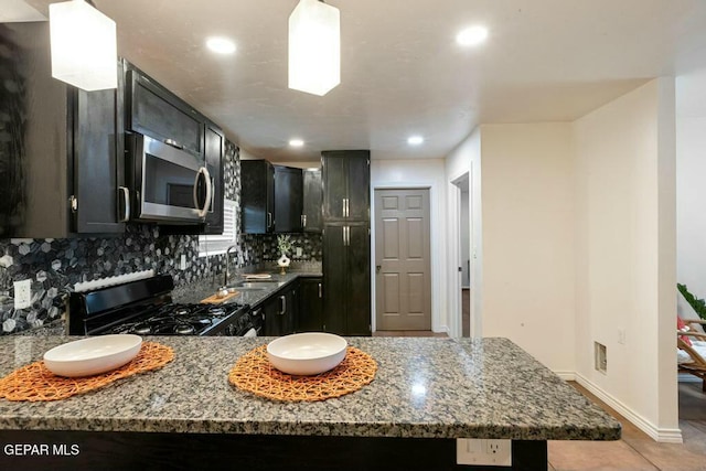 kitchen with stainless steel microwave, backsplash, black range with gas stovetop, stone counters, and a sink