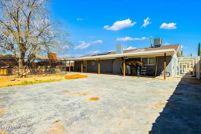 back of property with a patio area, roof mounted solar panels, central AC, and fence