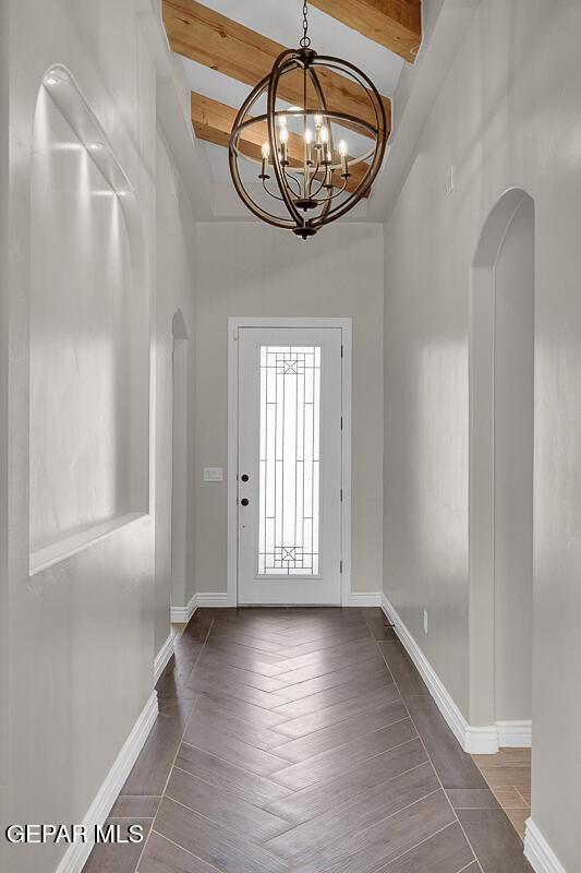 foyer entrance featuring arched walkways, beamed ceiling, and an inviting chandelier