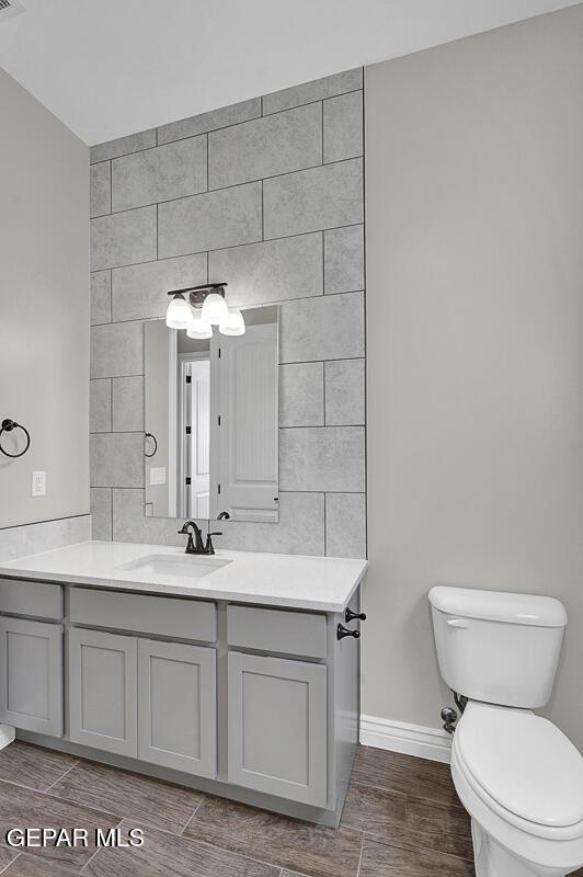 bathroom with toilet, vanity, tile walls, baseboards, and wood tiled floor