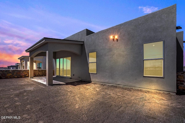 back of house at dusk featuring stucco siding and a patio