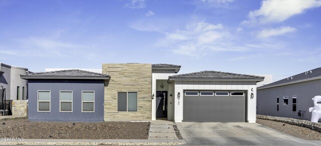 prairie-style house featuring concrete driveway, a garage, and stone siding