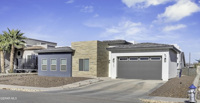 view of front of property featuring a garage, driveway, a trampoline, and stone siding