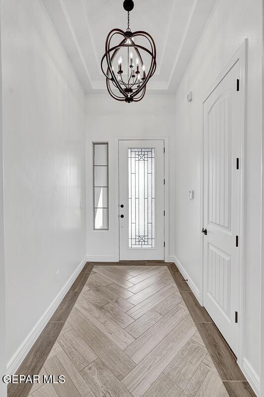 foyer entrance with baseboards, a raised ceiling, an inviting chandelier, and wood finished floors