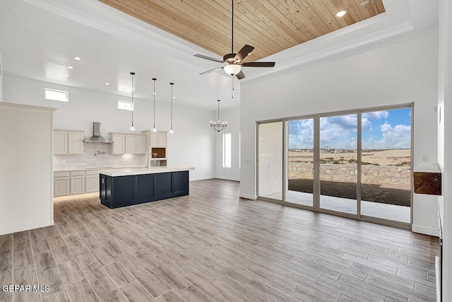 kitchen featuring open floor plan, light wood-type flooring, light countertops, wall chimney exhaust hood, and a sink