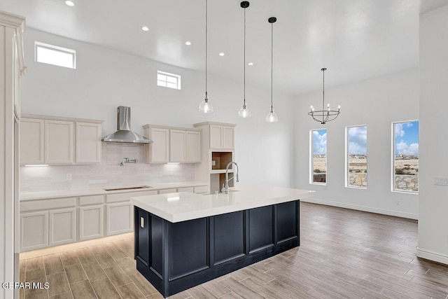 kitchen with wood tiled floor, stovetop, a sink, decorative backsplash, and wall chimney range hood