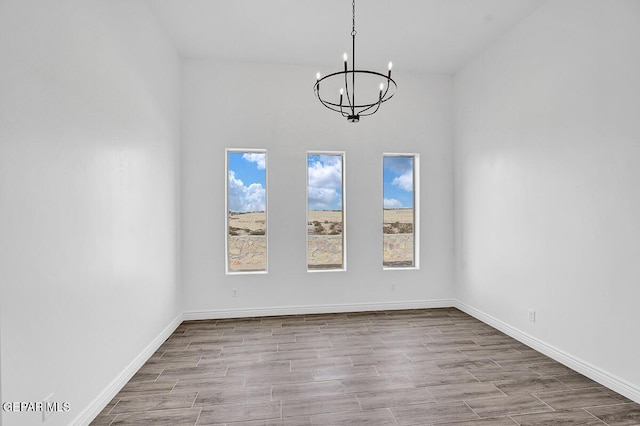 spare room with wood finished floors, baseboards, and a chandelier