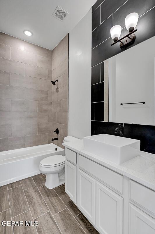 full bathroom featuring visible vents, wood finish floors, washtub / shower combination, toilet, and vanity