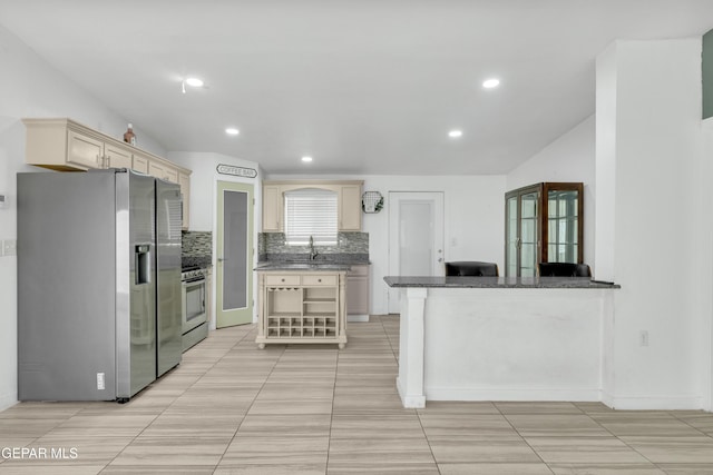 kitchen with decorative backsplash, lofted ceiling, cream cabinetry, and stainless steel appliances