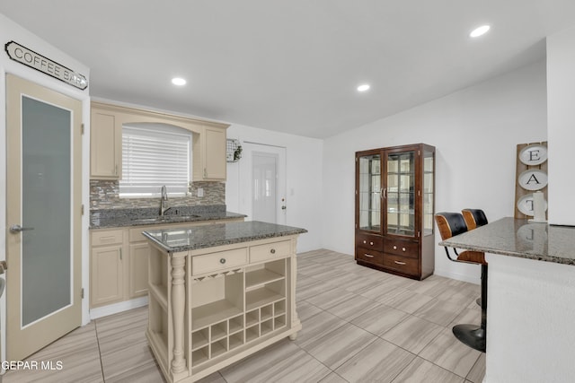 kitchen with decorative backsplash, dark stone countertops, cream cabinets, and a sink