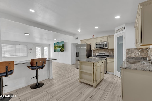 kitchen with lofted ceiling, a sink, cream cabinetry, appliances with stainless steel finishes, and tasteful backsplash