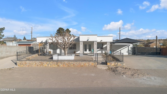 view of front facade featuring a fenced front yard, stucco siding, french doors, and concrete driveway