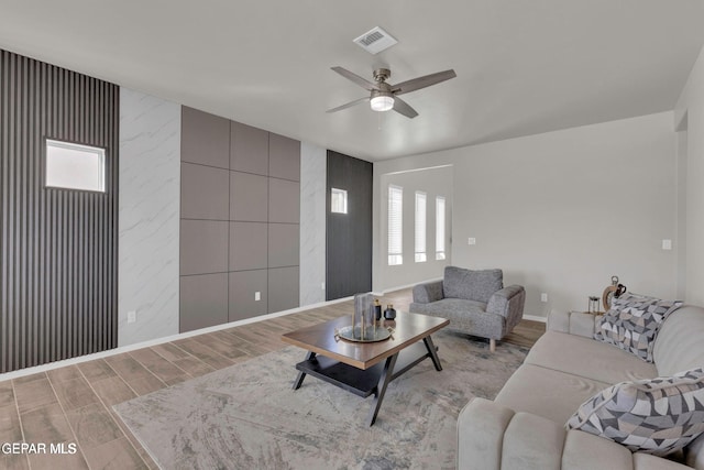 living room featuring a ceiling fan, wood finished floors, visible vents, and baseboards