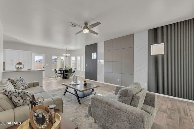 living room with visible vents, ceiling fan with notable chandelier, baseboards, and light wood-style floors