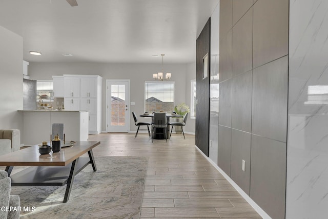 hall featuring wood finish floors, baseboards, and a notable chandelier