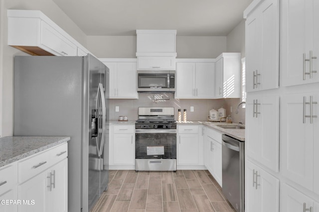 kitchen featuring wood finish floors, a sink, stainless steel appliances, white cabinets, and tasteful backsplash