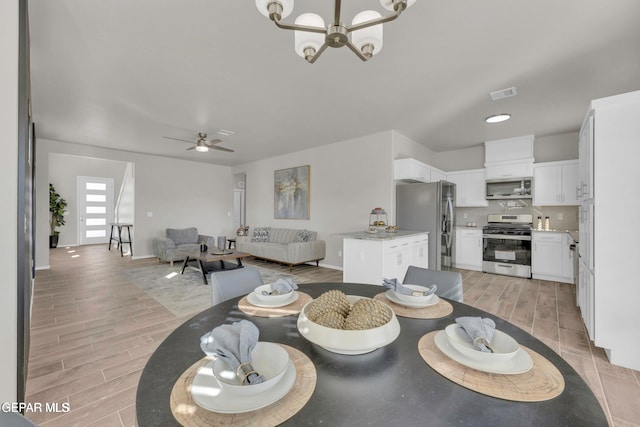 dining area with baseboards, ceiling fan with notable chandelier, visible vents, and wood finish floors