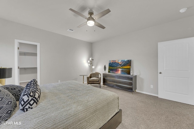 bedroom featuring a spacious closet, visible vents, baseboards, carpet floors, and a ceiling fan