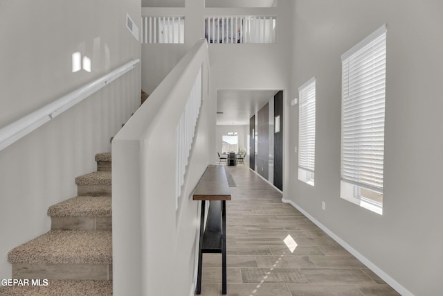 stairs featuring baseboards, visible vents, a towering ceiling, and wood tiled floor