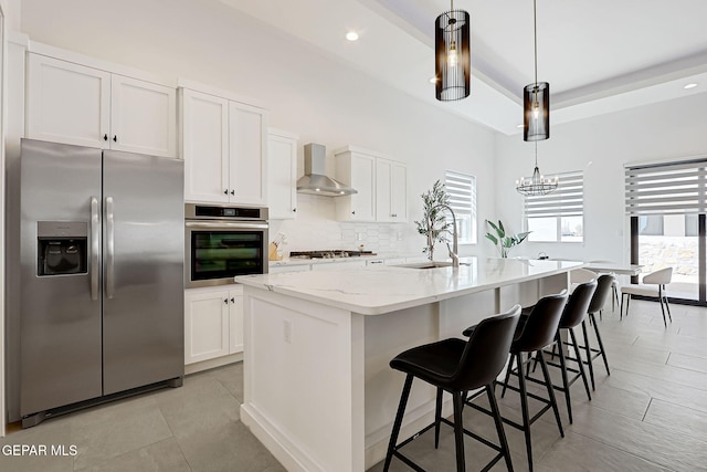 kitchen with light stone counters, stainless steel appliances, white cabinetry, wall chimney exhaust hood, and tasteful backsplash