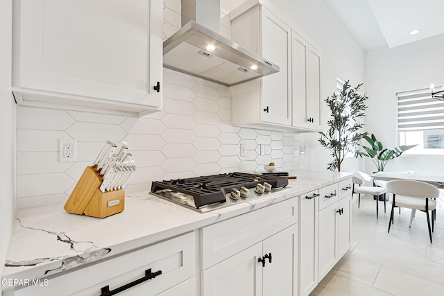 kitchen with light stone counters, white cabinetry, stainless steel gas stovetop, wall chimney exhaust hood, and decorative backsplash