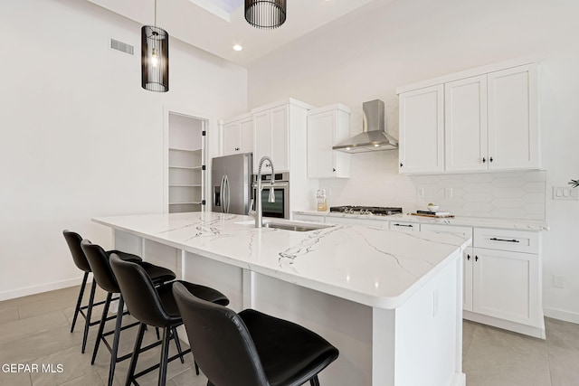 kitchen featuring backsplash, appliances with stainless steel finishes, white cabinets, wall chimney exhaust hood, and a sink