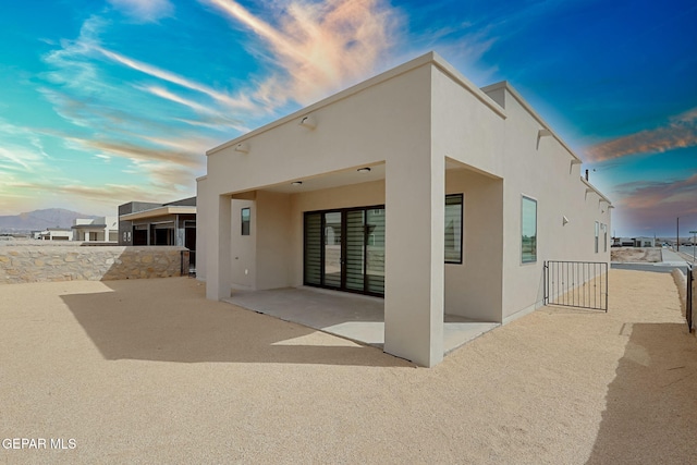 back of property at dusk with a patio area, stucco siding, and fence