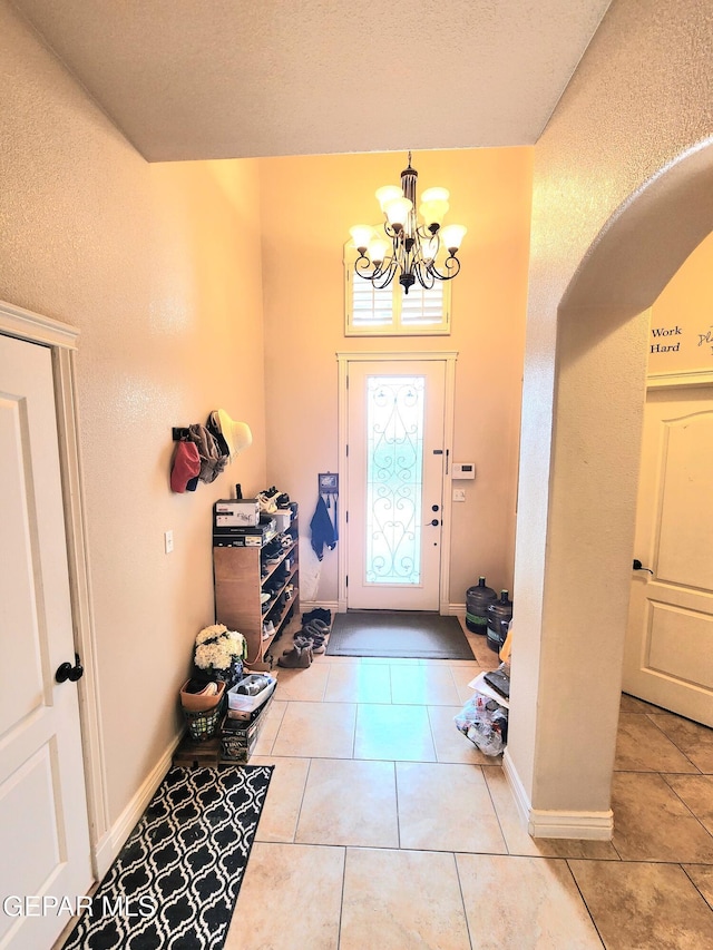 foyer entrance with tile patterned floors, a notable chandelier, baseboards, and arched walkways