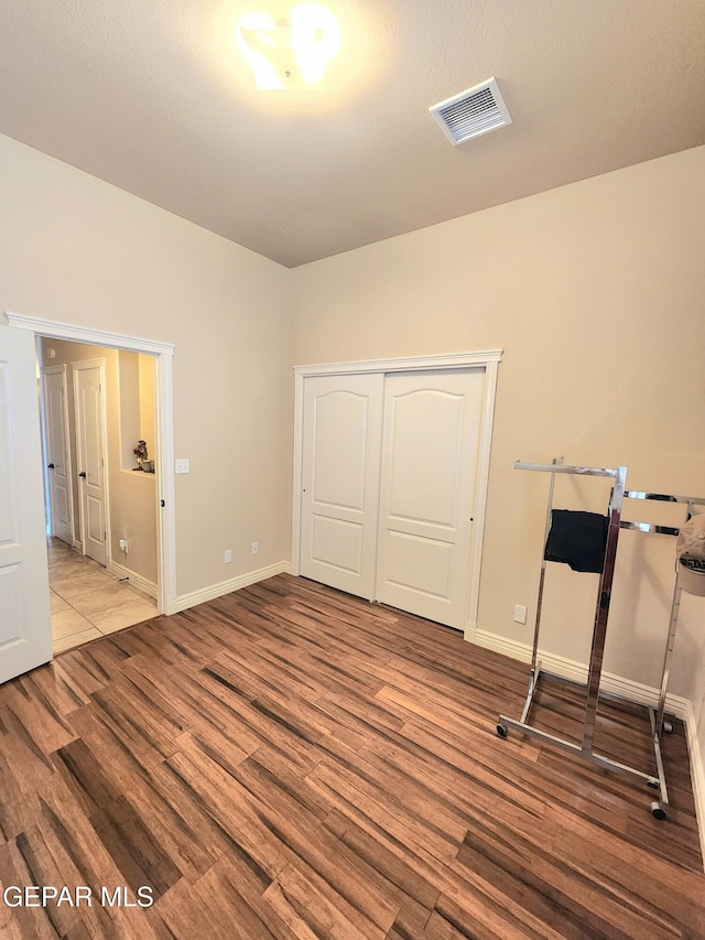 unfurnished bedroom featuring a closet, visible vents, baseboards, and wood finished floors