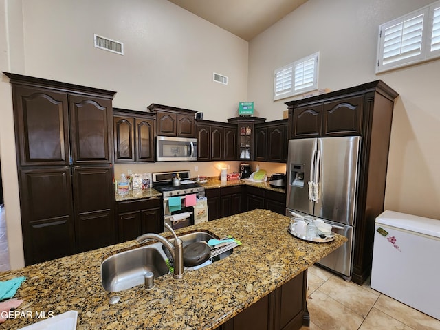 kitchen featuring light stone countertops, visible vents, stainless steel appliances, dark brown cabinets, and a towering ceiling