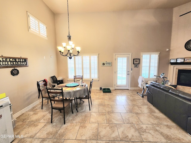 dining room with baseboards, light tile patterned floors, a fireplace, a high ceiling, and a notable chandelier