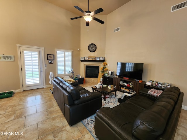 living area with a tiled fireplace, visible vents, baseboards, and ceiling fan