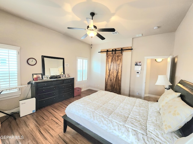 bedroom with a barn door, wood finished floors, visible vents, and baseboards