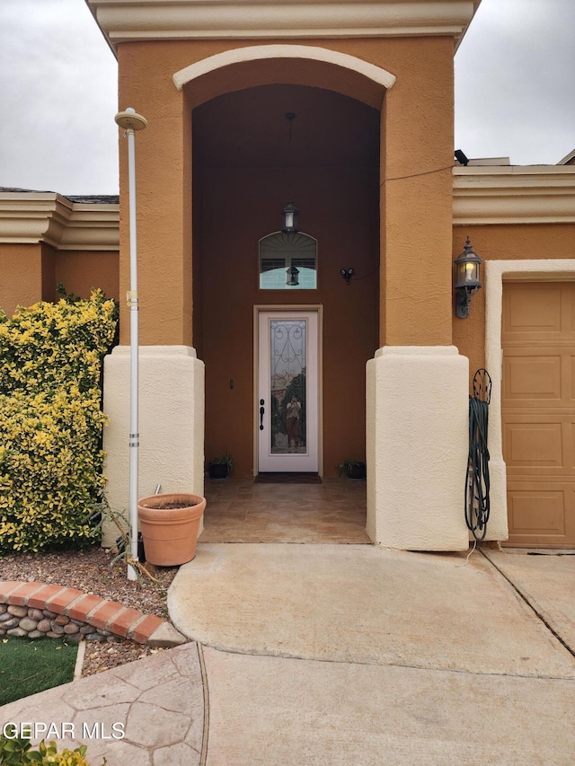 entrance to property with stucco siding, a garage, and driveway