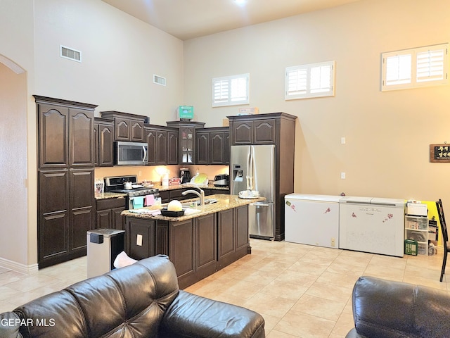 kitchen with dark brown cabinets, appliances with stainless steel finishes, arched walkways, a towering ceiling, and light tile patterned flooring