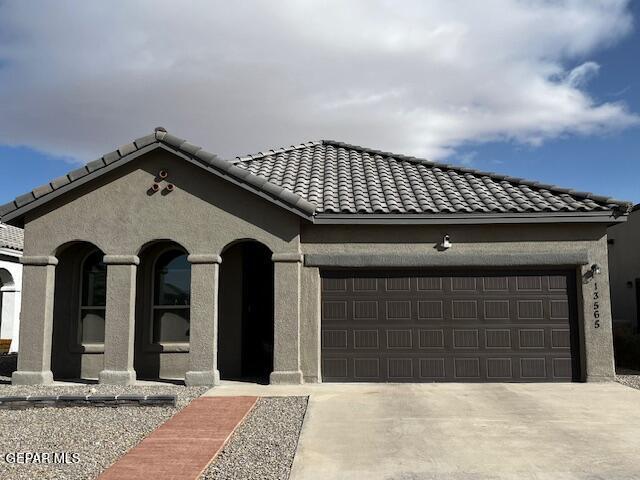 view of front of home featuring stucco siding, driveway, a tile roof, and a garage