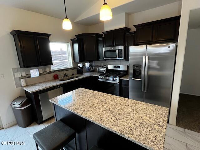 kitchen with pendant lighting, light stone counters, a sink, backsplash, and stainless steel appliances