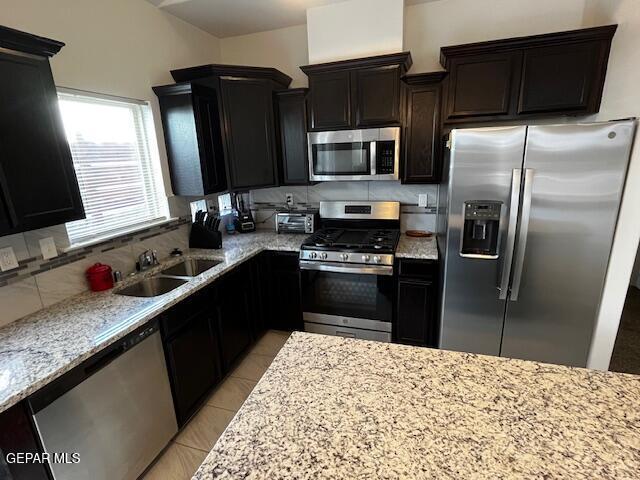 kitchen featuring a sink, stainless steel appliances, light stone counters, and backsplash