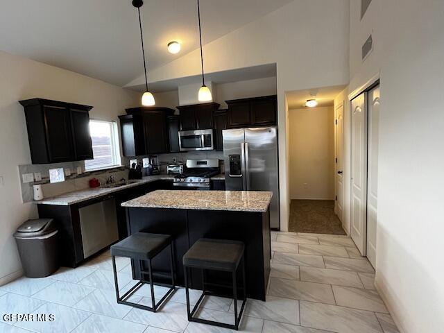 kitchen with visible vents, light stone counters, dark cabinetry, a center island, and appliances with stainless steel finishes