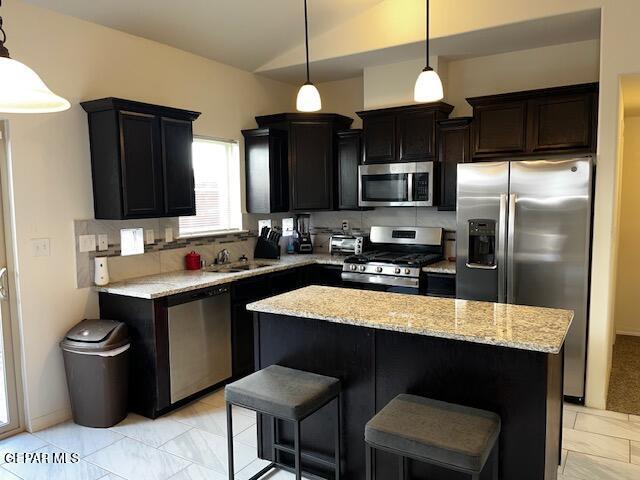 kitchen with a kitchen island, light stone countertops, vaulted ceiling, stainless steel appliances, and a sink