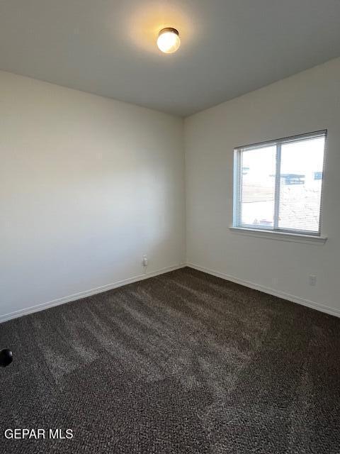 empty room featuring baseboards and dark colored carpet