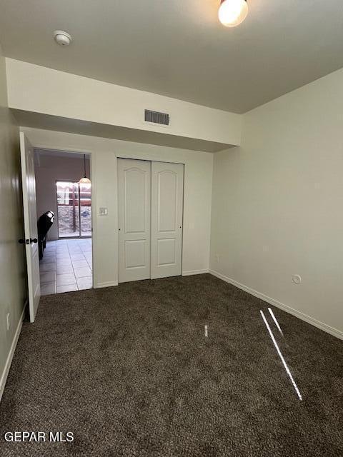 unfurnished bedroom featuring baseboards, visible vents, carpet floors, tile patterned flooring, and a closet