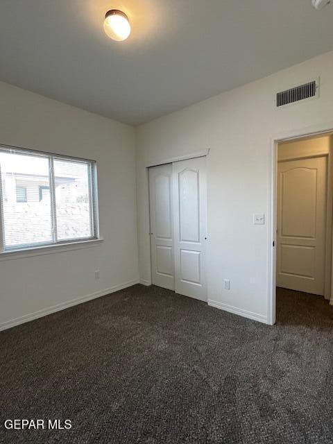 unfurnished bedroom with a closet, baseboards, visible vents, and dark carpet