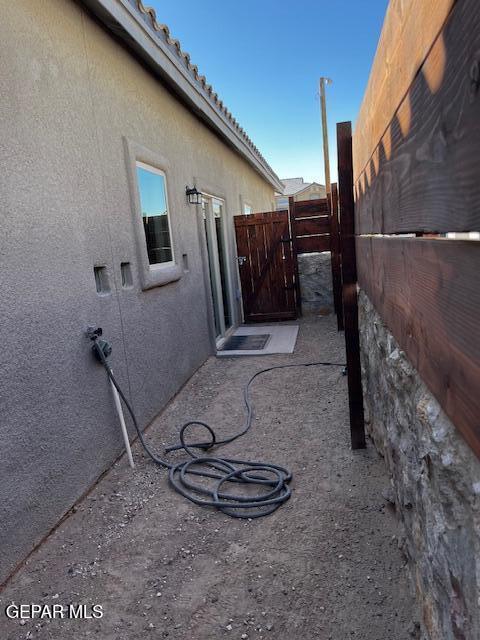 view of side of property with stucco siding, a tile roof, a patio, and fence