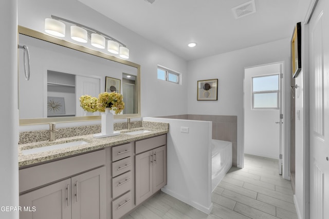 full bathroom featuring a sink, visible vents, a bath, and double vanity