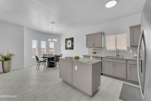 kitchen featuring tasteful backsplash, visible vents, gray cabinetry, a center island, and a sink