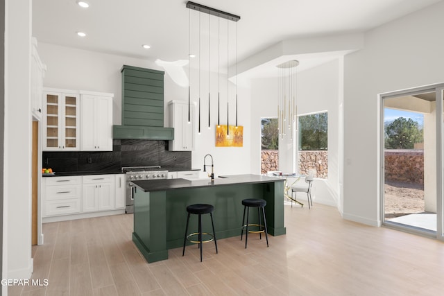 kitchen with high end stove, backsplash, dark countertops, white cabinets, and wall chimney range hood