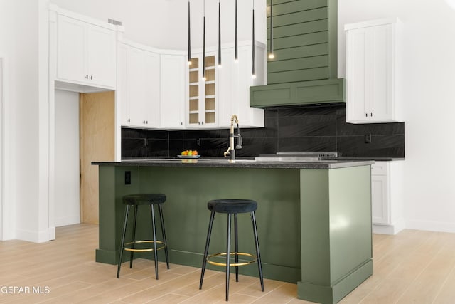 kitchen featuring tasteful backsplash, glass insert cabinets, a kitchen breakfast bar, light wood-style floors, and white cabinetry