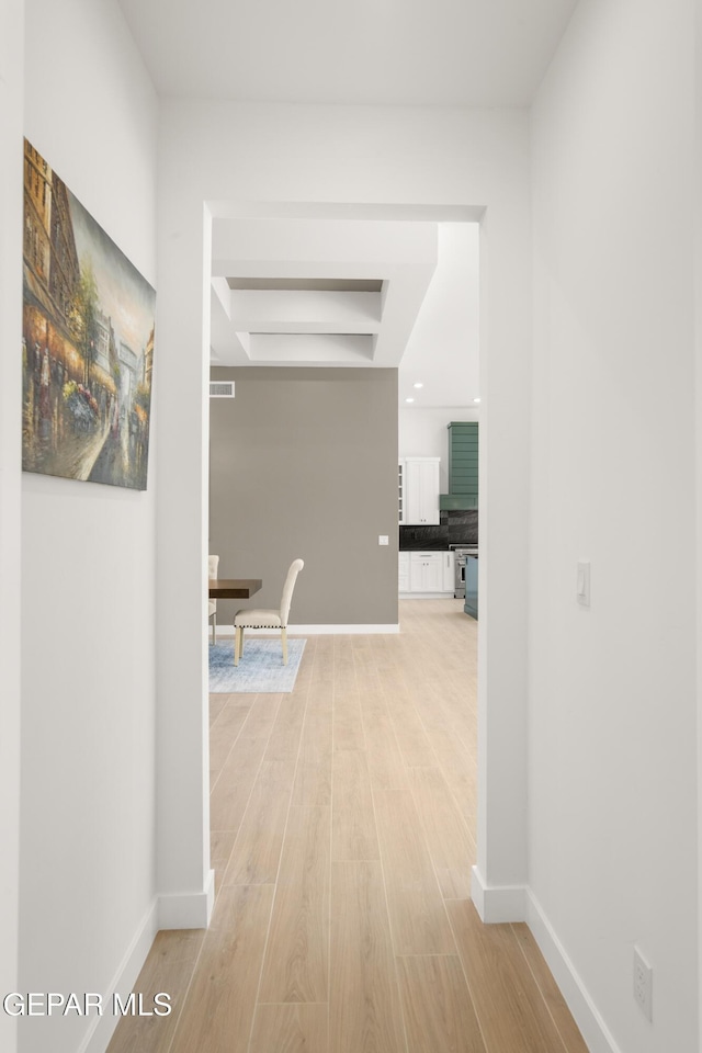 corridor featuring a raised ceiling, baseboards, and light wood finished floors